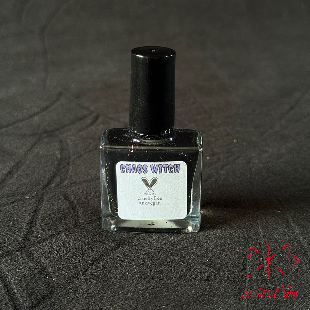 Chaos Witch Nail Varnish Scarlet in Chains and Radioactive Unicorn Collaboration, A small square glass bottle of nail polish or ink with a black cap and a white label reading 'CHAOS WITCH', placed on a dark textured surface.