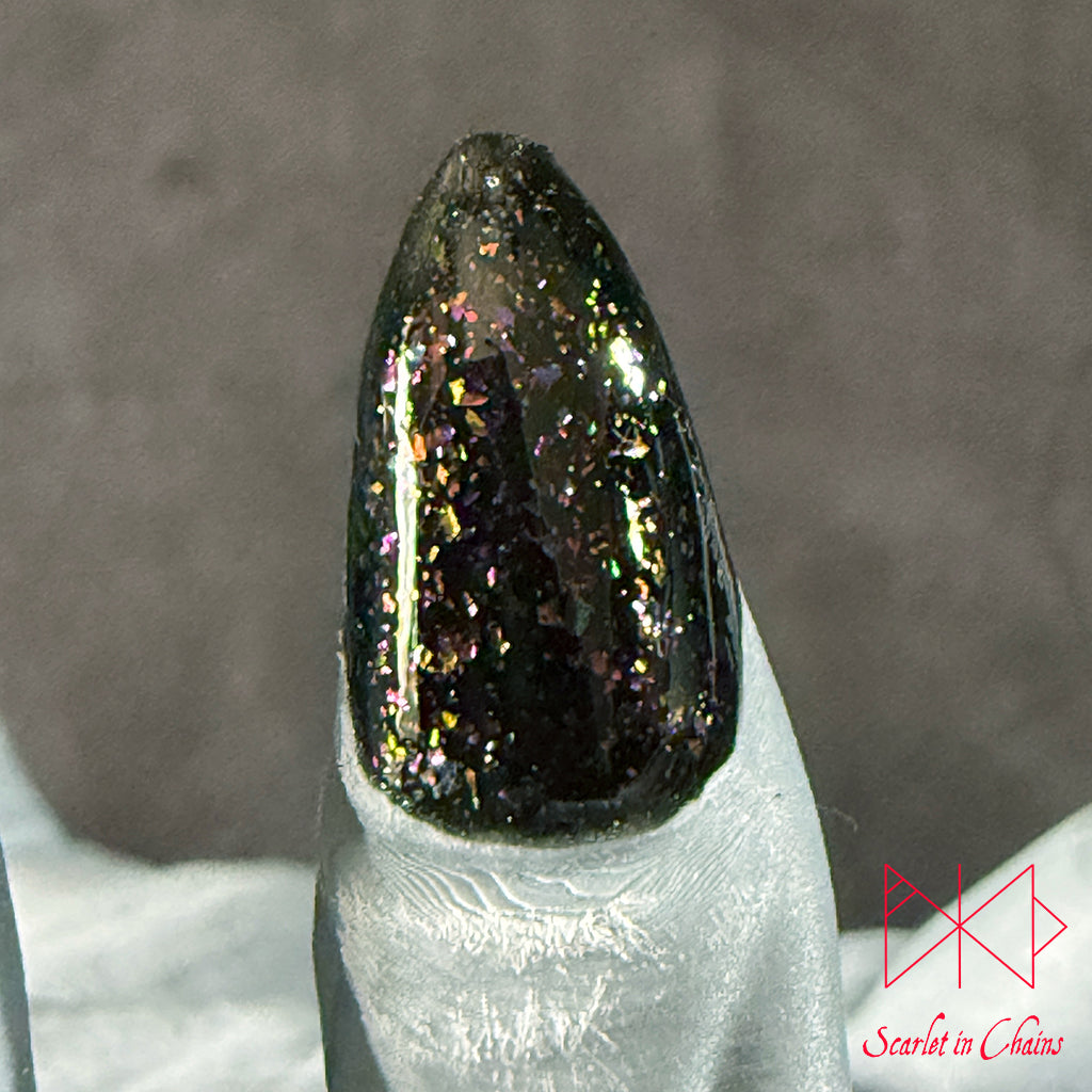 Chaos Witch Nail Varnish Scarlet in Chains and Radioactive Unicorn Collaboration, A close-up of a glossy black nail tip filled with dense iridescent holographic glitter, mounted on a white nail form against a soft grey background.
