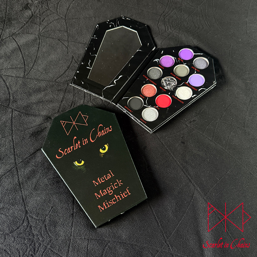 Metal Magic Mischief Makeup Pallet A Scarlet in Chains and Radioactive Unicorn Collaboration. A gothic-themed metal makeup palette set by Scarlet in Chains, featuring a black coffin-shaped case with a mirror and a second closed case displaying the brand name and cat-eye graphic from our Sabra, alongside an open palette showing 12 metallic eyeshadow pans in various colors.