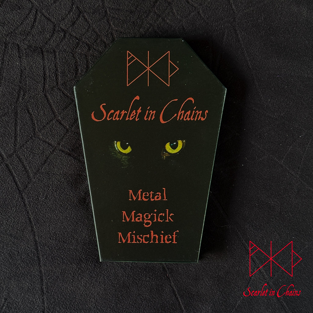 Metal Magic Mischief Makeup Pallet A Scarlet in Chains and Radioactive Unicorn Collaboration. A black coffin-shaped cover with red gothic text reading 'Scarlet in Chains' and 'Metal Magick Mischief,' plus yellow eyes our Sabra cat, shown on a dark textured background.