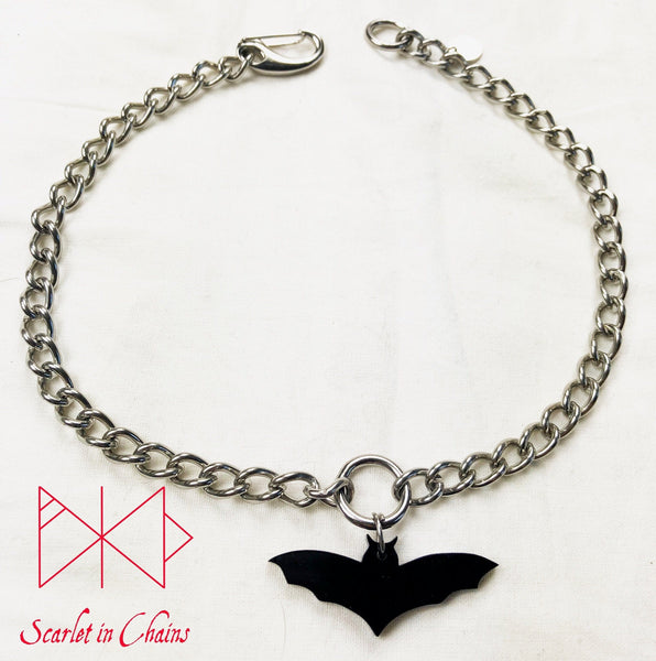 Bat choker flat on white background. Stainless steel chain choker with stainless steel o ring at its centre with a black perspex bat pendant hung from the O ring. Finished with our easy to use stainless steel clasp and hand stamped stainless steel logo tag.